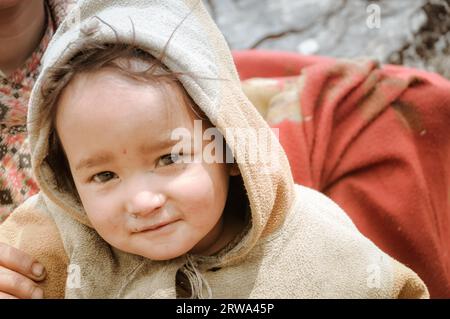Dolpo, Nepal, um Juni 2012: Ein kleines braunhaariges Kind im braunen Pullover schaut neugierig auf Fotokamera mit glitzernden braunen Augen in schön Stockfoto