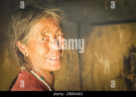 Dolpo, Nepal, um Mai 2012: Alte gebürtige Frau mit faltigem Gesicht trägt Ohrringe und Halskette aus Perlen in Dolpo, Nepal. Dokumentarisches Editorial Stockfoto