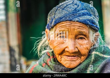 Beni, Nepal, um Mai 2012: Foto einer alten Frau mit Falten und Piercing, die blaue Kappe trägt und in den Straßen von Beni, Nepal, auf Fotokamera schaut. Stockfoto