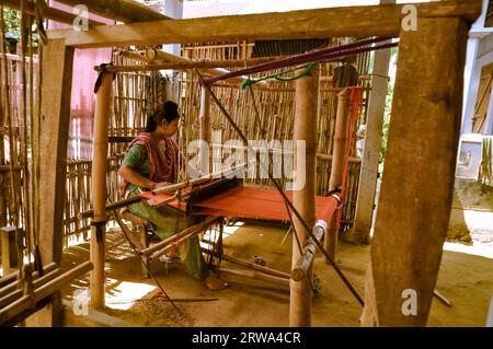 Srimongal, Bangladesch, um Juli 2012: Junge schwarzhaarige Frau sitzt und webt auf einfachen Holzwebstuhl in Srimongal, Bangladesch. Dokumentarisches Editorial Stockfoto