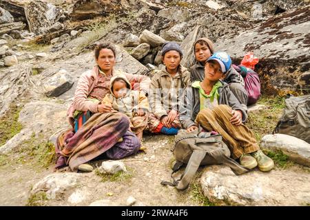 Dolpo, Nepal, um Juni 2012: Braunhaarige Ureinwohnerin sitzt mit ihren Kindern mit Jacken auf Stein und sie posieren vor der Kamera in schöner Schönheit Stockfoto