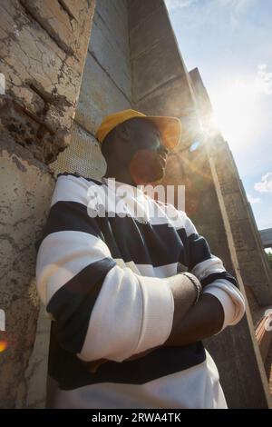 Modenporträt mit niedrigem Winkel von trendigem schwarzen Mann, der im Sonnenlicht mit Lichtreflexen wegschaut Stockfoto