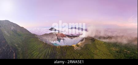 Panorama aus der Vogelperspektive von Felsklippen am Vulkan Kawah Ijen mit türkisfarbenem Schwefelwassersee bei Sonnenaufgang. Fantastischer Blick auf die Naturlandschaft in Ost-Java, Indon Stockfoto