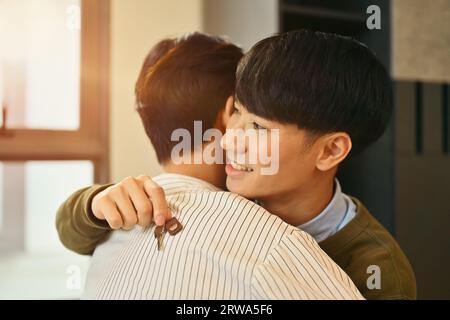 Ein schwules Paar, das nach dem Immobilienkauf den Schlüssel hält und draußen in seinem neuen Haus steht. LGBTQ und Relocation Concept Stockfoto