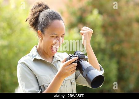 Aufgeregter schwarzer Fotograf, der im Park ein gutes Ergebnis überprüft Stockfoto