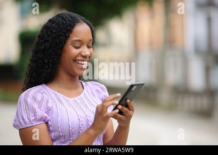 Glückliche schwarze Frau mit Smartphone auf der Straße zu Fuß Stockfoto