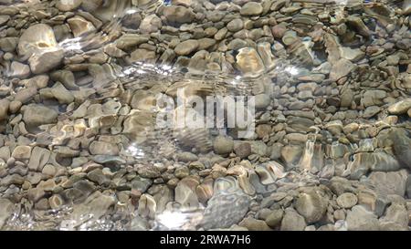 Die Sonne wirbelt und plätschert auf klarem, fließendem Wasser mit Kieselsteinen auf dem Boden Stockfoto