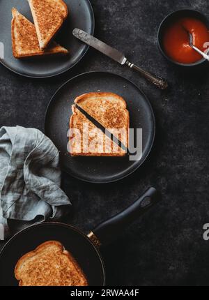 Draufsicht auf gegrillte Käse-Sandwiches und Suppe auf schwarzem Hintergrund. Stockfoto