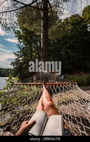 Beine einer Frau, die in einer Hängematte mit Buch am Sommertag liegt. Stockfoto