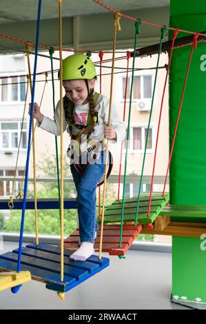 Kinderseilbahn im Spielzimmer passiert das kleine Mädchen die Seilbahn, die aktive und körperliche Entwicklung des Kindes. Stockfoto