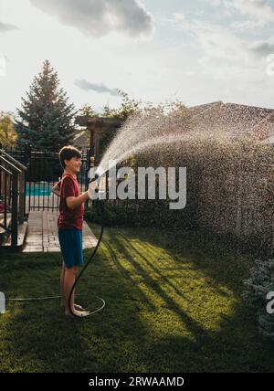 Junge, die den Garten im Garten mit Schlauch am Sommertag bewässern. Stockfoto
