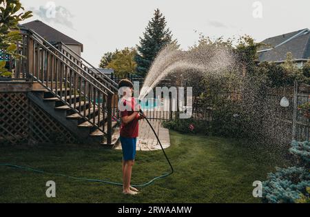 Junge, die den Garten im Garten mit Schlauch am Sommertag bewässern. Stockfoto
