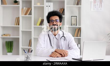 Porträt eines jungen indischen Arztes, der lächelt und die Kamera in einem weißen Mantel mit Stethoskop anschaut. Nahansicht. Stockfoto