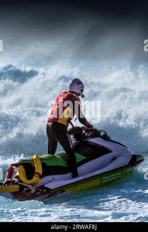 Ein RNLI-Rettungsschwimmer, der im Dienst auf einem Jetski in Fistral in Newquay in Cornwall in England im Vereinigten Königreich sitzt. Stockfoto