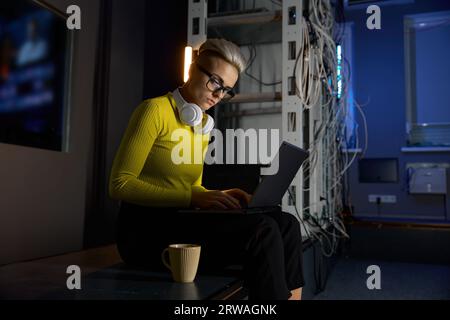 Junge Frau, die mit Laptop im Serverraum arbeitet Stockfoto