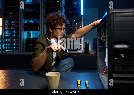 Junger IT-Techniker, der Taschenlampen verwendet, um Probleme mit dem Computer in modernen Rechenzentren zu finden Stockfoto