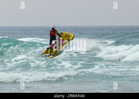 RNLI-Rettungsschwimmer auf Jetski auf dem Weg in die raue See vor Perranporth Beach, Cornwall, Großbritannien. Rettungsschwimmer, der auf See reitet Stockfoto