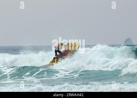 RNLI-Rettungsschwimmer auf Jetski auf dem Weg in die raue See vor Perranporth Beach, Cornwall, Großbritannien. Rettungsschwimmer, der auf See reitet Stockfoto