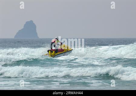 RNLI-Rettungsschwimmer auf Jetski auf dem Weg in die raue See vor Perranporth Beach, Cornwall, Großbritannien. Rettungsschwimmer, der auf See reitet Stockfoto