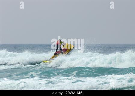 RNLI-Rettungsschwimmer auf Jetski auf dem Weg in die raue See vor Perranporth Beach, Cornwall, Großbritannien. Rettungsschwimmer, der auf See reitet Stockfoto