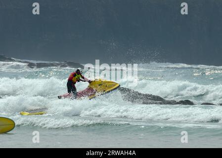 RNLI-Rettungsschwimmer auf Jetski auf dem Weg in die raue See vor Perranporth Beach, Cornwall, Großbritannien. Rettungsschwimmer, der auf See reitet Stockfoto