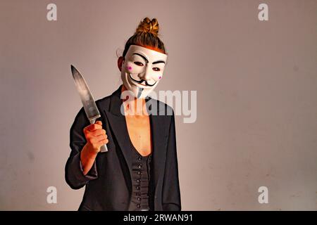 Frau mit einer anonymen Maske in einer schwarzen Anzugjacke, mit einem Messer in der Hand, vorbereitet für die Halloween-Party Stockfoto