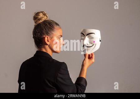 Frau mit einer anonymen Maske in einer schwarzen Anzugjacke, mit einem Messer in der Hand, vorbereitet für die Halloween-Party Stockfoto