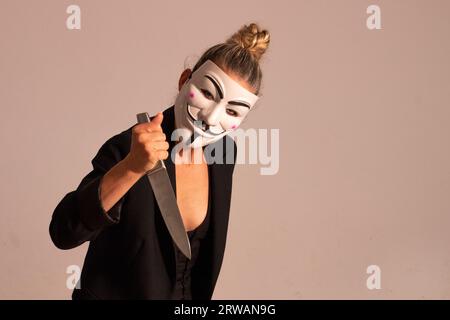 Frau mit einer anonymen Maske in einer schwarzen Anzugjacke, mit einem Messer in der Hand, vorbereitet für die Halloween-Party Stockfoto