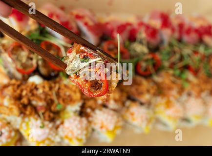 Sushi-Rollen verschiedener Art in einer Bastelbox, Hände halten ein Stück mit Holzstäbchen. Lieferung, Mitnahme Stockfoto