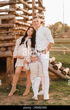 Eine stilvolle Familie auf dem Land bei Sonnenuntergang. Eine schwangere Frau mit ihrem Mann und Sohn in der Natur. Stockfoto