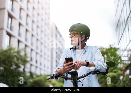 Reifer Mann, der ein Mobiltelefon benutzt, während er mit dem Fahrrad in der Stadt fährt Stockfoto