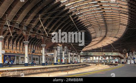 Ein Bahnsteig am Bahnhof York. Das Eisendach aus dem 19. Jahrhundert kurvt um den Bahnhof und Züge warten auf Anschlussgleise. Eine Fußgängerbrücke überquert die Schienen Stockfoto