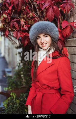 Mädchen in rotem Mantel mit Pelzmütze, die im Schnee posiert Stockfoto