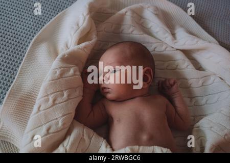 Das kleine süße Neugeborene liegt in einer weißen Decke auf dem Bett. Stockfoto