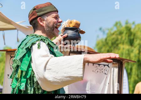 Mittelalterliche Puppenspielerin in einem grünen Kostüm, die im Sommer bei einer Reenactment-Veranstaltung in Sandwich Town in kent mit Marionette auftritt. Stockfoto