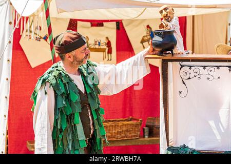 Mittelalterliche Puppenspielerin in einem grünen Kostüm, die im Sommer bei einer Reenactment-Veranstaltung in Sandwich Town in kent mit Marionette auftritt. Stockfoto
