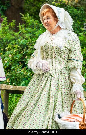 Ältere Frau in viktorianischen Kostümen eines grünen Kleides und einer Mütze mit einem Spitzenschal, die in einem Garten stehen. Broadstairs Dickens Woche. Stockfoto