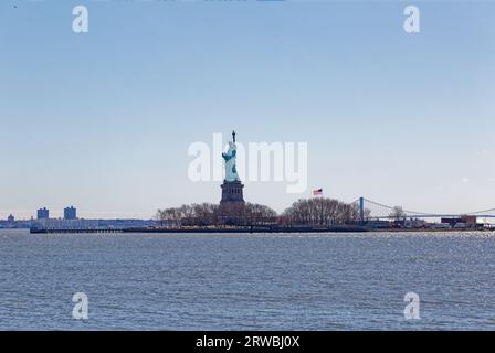Freiheitsstatue aus dem Liberty State Park, New Jersey: Die selten gesehene Seite von Lady Liberty. Die Verrazzano Narrows Bridge ist in der Ferne. Stockfoto