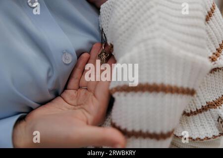 Hand eines Patenvaters, der das Brustkreuz des Babys während der Taufzeremonie in der orthodoxen Kirche hält. Nahaufnahme. Stockfoto