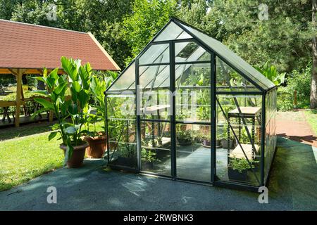 Gewächshaus im Garten. Kleines, kompaktes Glasgewächshaus für den Anbau von Blumen, Gemüse, Setzlingen verschiedener Pflanzen. Gartenarbeit. Wunderschönes Glashaus im Hof. Hobby kein Graben. Stockfoto