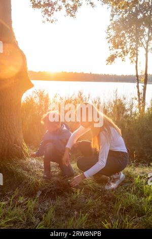 Erleben Sie die Magie eines herzerwärmenden Mutter-Sohn-Moments, während Sie sich auf eine faszinierende Entdeckungsreise durch die Natur begeben, während Sie einen ruhigen Sonnenuntergang genießen. In einer malerischen Umgebung an einem ruhigen Waldsee weckt die liebevolle Führung der Mutter die Neugier und das Staunen ihres Sohnes. Gemeinsam teilen sie eine liebevolle Erinnerung, gefüllt mit Entdeckung, Liebe und der tiefen Schönheit der natürlichen Welt. Diese berührende Szene fängt das Wesen der Familie, der Zweisamkeit und der anhaltenden Magie der Natur ein. Bezaubernde Erkundung des Sonnenuntergangs: Mutter und Sohn Bonding. Hochwertige Fotos Stockfoto