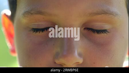 Kindergesicht-Close-up-Augenschließen in der Meditation. Junge, der Augen öffnet, lächelt vor der Kamera, Makroaufnahme Stockfoto