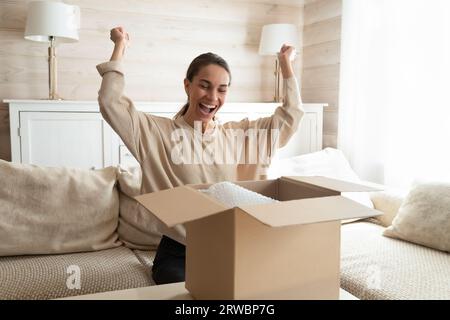Aufgeregte Frau, die das Paket auspackt und in eine offene Pappschachtel schaut Stockfoto