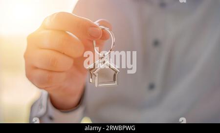 Selektiver Fokus auf einen Schlüsselanhänger in Form eines Hauses für ein neues Zuhause, das von einem Immobilienmakler gehalten wird, der die Hausschlüssel übergibt. Immobilien und Bauwesen Stockfoto