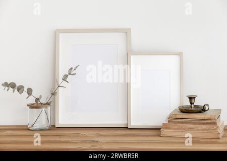 Holzrahmen auf einem Holztisch mit einem Vintage-Kerzenleuchter auf antiken Büchern, eine Glasvase mit Eukalyptus auf weißem Wandhintergrund. Skandinavisch Stockfoto