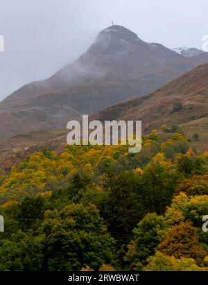 Niedriger Winkel des fernen Berggipfels, bedeckt mit Dunst, der im Herbst über bunten Bäumen in den französischen Alpen fließt Stockfoto