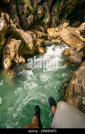 Von oben bepflanzte, nicht erkennbare männliche Touristen, die durchsichtiges, klares, plätscherndes Flusswasser bewundern, das durch die felsige, raue Höhle Cueva del gato fließt Stockfoto