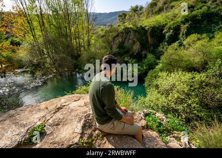 Von oben Blick auf den männlichen Touristen, der das durchsichtige, klare, plätschernde Flusswasser bewundert, das durch die felsige, raue Höhle Cueva del gato in Benaoján fließt, Stockfoto