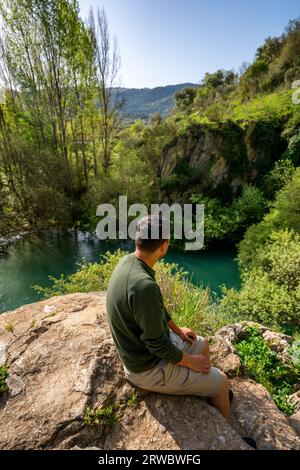 Von oben Blick auf den männlichen Touristen, der das durchsichtige, klare, plätschernde Flusswasser bewundert, das durch die felsige, raue Höhle Cueva del gato in Benaoján fließt, Stockfoto