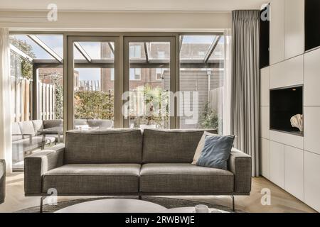 Komfortables Sofa mit Kissen auf hellem Wohnzimmer gegen großes Fenster neben dem Garten in einem modernen Apartment Stockfoto